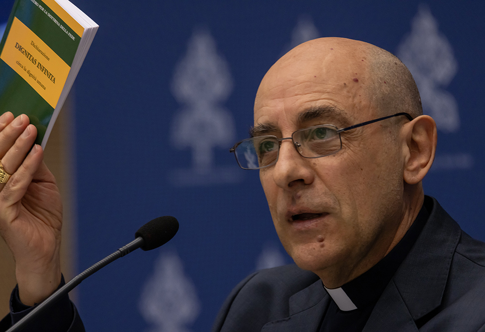 Cardinal Víctor Manuel Fernández, prefect of the Dicastery for the Doctrine of the Faith, holds up a copy of the dicastery's declaration, Dignitas Infinita ("Infinite Dignity") on human dignity during a news conference April 8 at the Vatican press office. (CNS/Pablo Esparza)