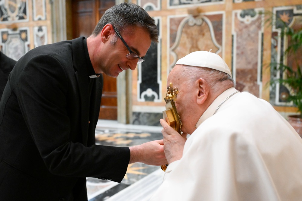 Pope Francis kisses a gold reliquary while seated. 