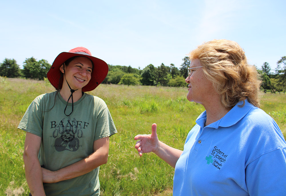 En el campo, con los pastizales al fondo, conversan la hermana Karen Burkec, oordinadora de las iniciativas sobre la tierra de las Hermanas de San José de Brentwood, y la ecologista del paisaje Amanda Furcall. 