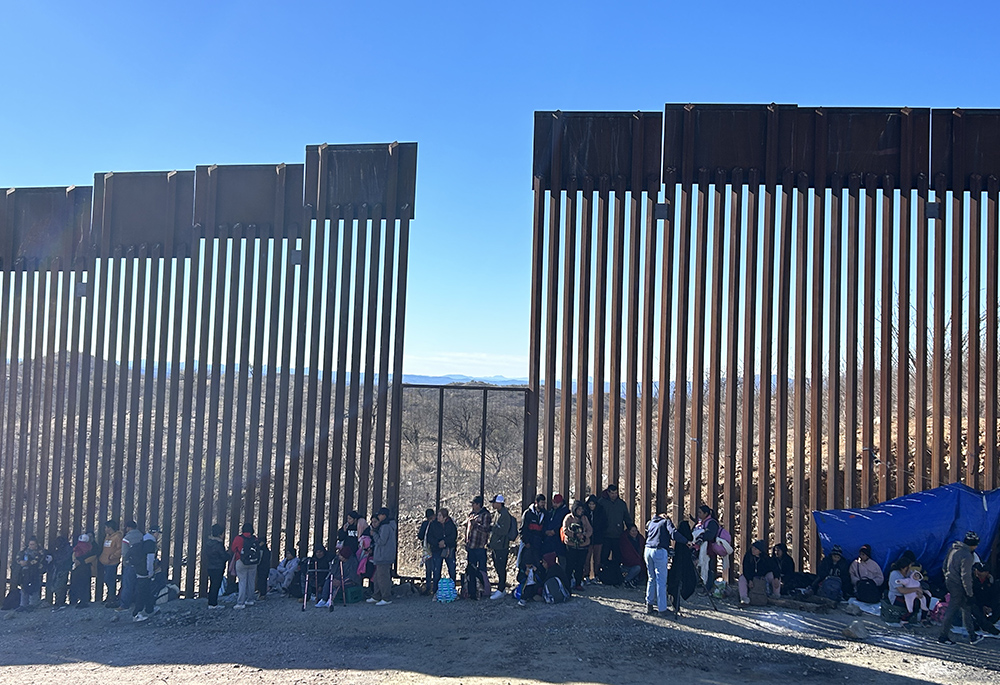 Asylum-seekers standing at the U.S.-Mexico border wall (Peter Tran)