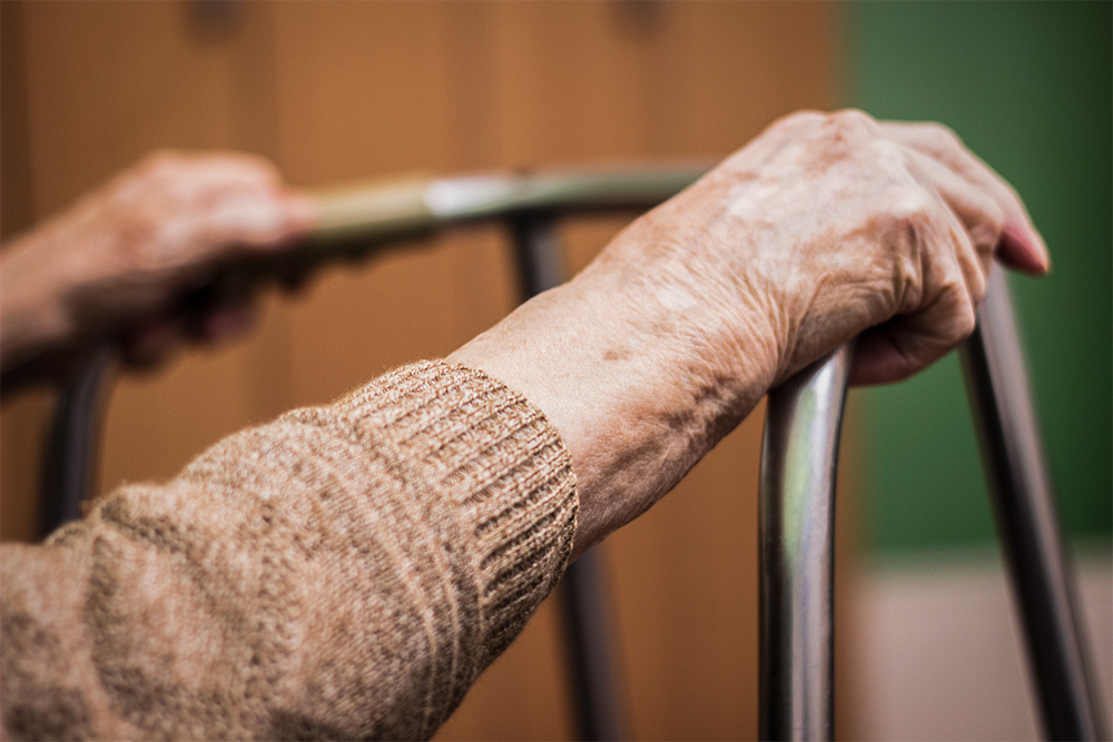 An elderly person's hands rest on a walker (Dreamstime/Sanjagrujic)