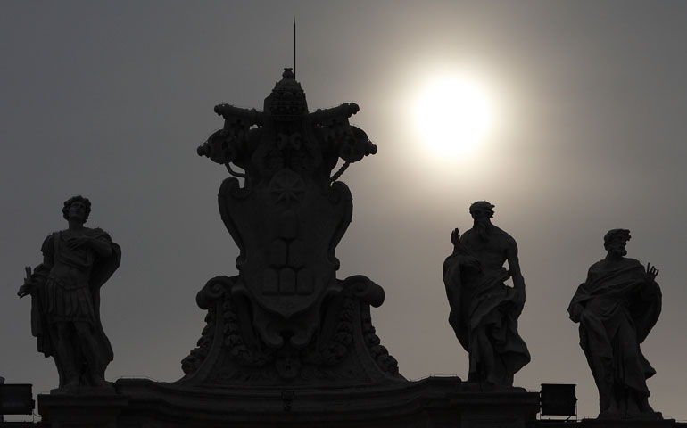 A papal tiara and keys are silhouetted between saints on the colonnade in the morning in St. Peter’s Square at the Vatican March 1. (CNS/Paul Haring)