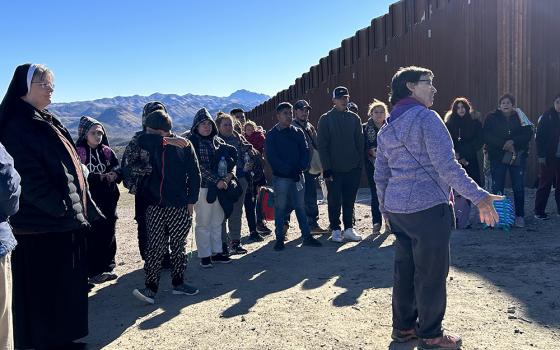 Sr. Judy Bourg (purple jacket) stands with asylum-seekers who entered the United States through an opening in the U.S.-Mexico border wall. Bourg welcomed each of them, then gathered them in a circle, and said, "We are happy that you are here." To Bourg's left is Sr. Maria Louis Edwards.