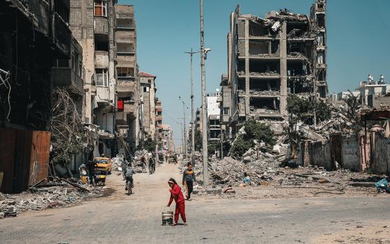A child carries a bucket along a row of destroyed buildings March 16 in Gaza City. (OSV News/Courtesy of Caritas Poland)