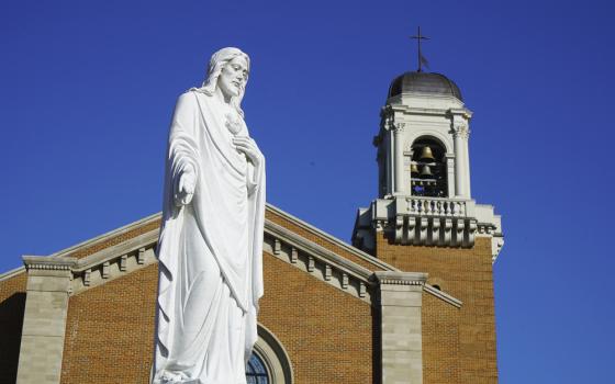 Large statue of Jesus against cathedral's spire and blue sky