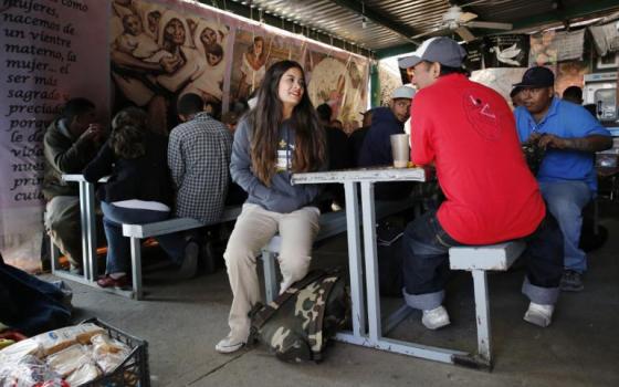 Nicole Davison sits down to chat with a deported father after he finished dinner April 2 at the comedor, the kitchen and dining hall of the Centro de Atencion al Migrante Deportado, the Aid Center for Deported Migrants, in Nogales, Sonora. (Nancy Wiechec)