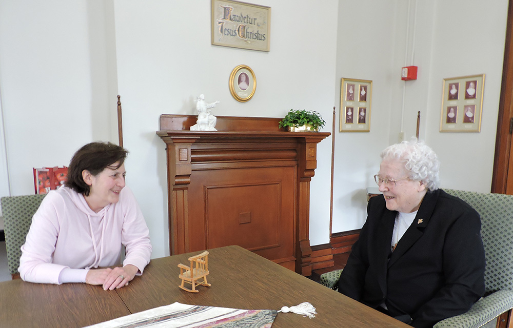 Dos religiosas conversan sentadas y apoyadas en una mesa marrón en el salón blanco de visitas del Convento de Nuestra Señora de los Ángeles, en Pensilvania.