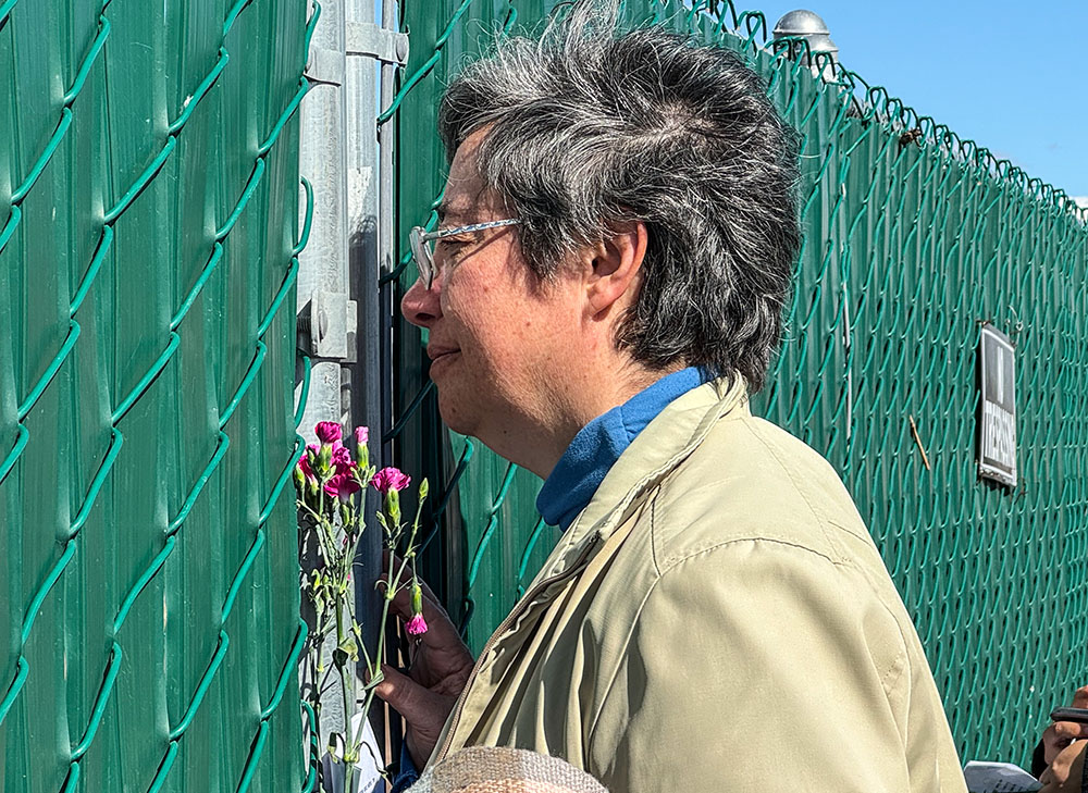 Sr. Clara Malo Castrillón, provincial of Mexico's Society of the Sacred Heart, looks through an opening in a fence where you can see tombs fenced off from the rest of Terrace Park Cemetery in Holtville, California, during a Feb. 7 stop. Sisters stopped to pray and threw flowers over the locked fence toward the bricks that serve as tombstones where remains include those of anonymous migrants. (GSR photo/Rhina Guidos) 