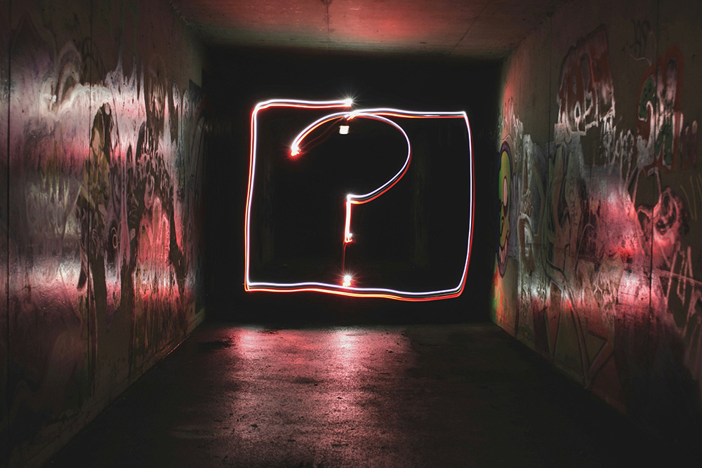 A question mark in light down a dark, graffitied hallway (Unsplash/Emily Morter)