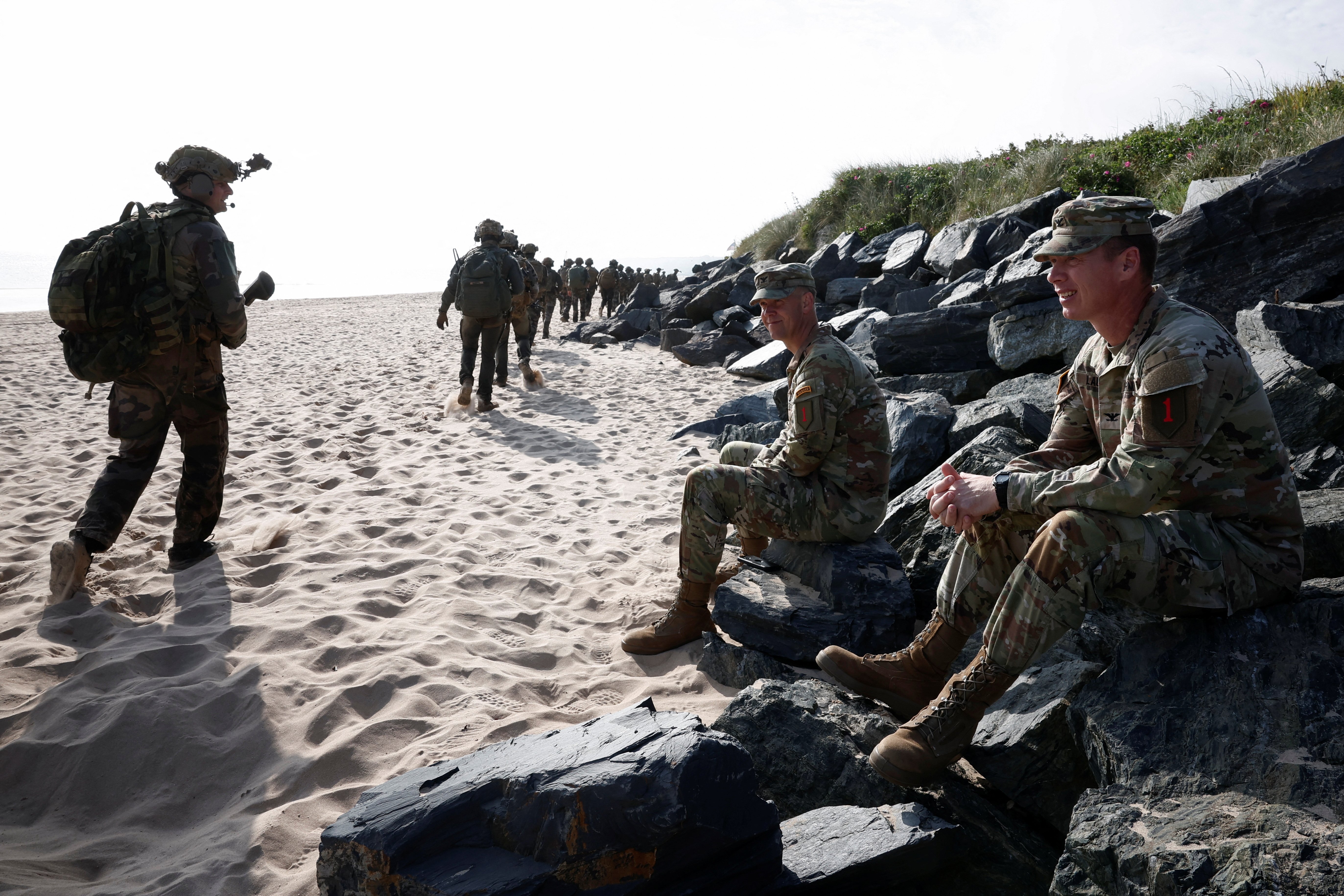 Soldiers sit and walk on beach. 
