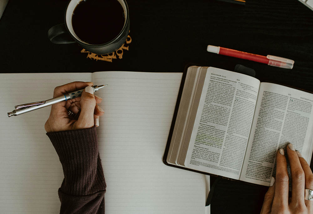 Una composición fotográfica muestra un plano cenital de una mujer escribiendo en un cuaderno, mientras revisa una Biblia. (Foto: Unsplash/Kelly Sikkema)