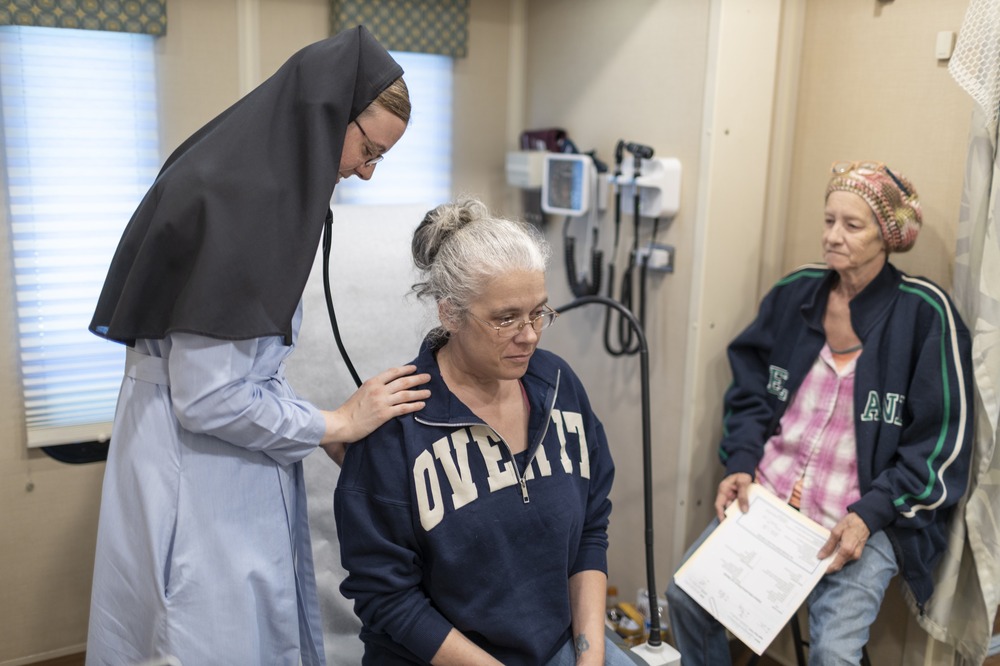 Sisters Mary Lisa, in habit, listens to patient's heart with stethoscope.