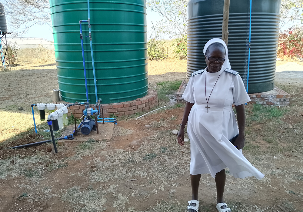 Precious Blood Sr. Caroline Busvumani stands in front of two water reservoirs called JoJo tanks. (Marko Phiri)