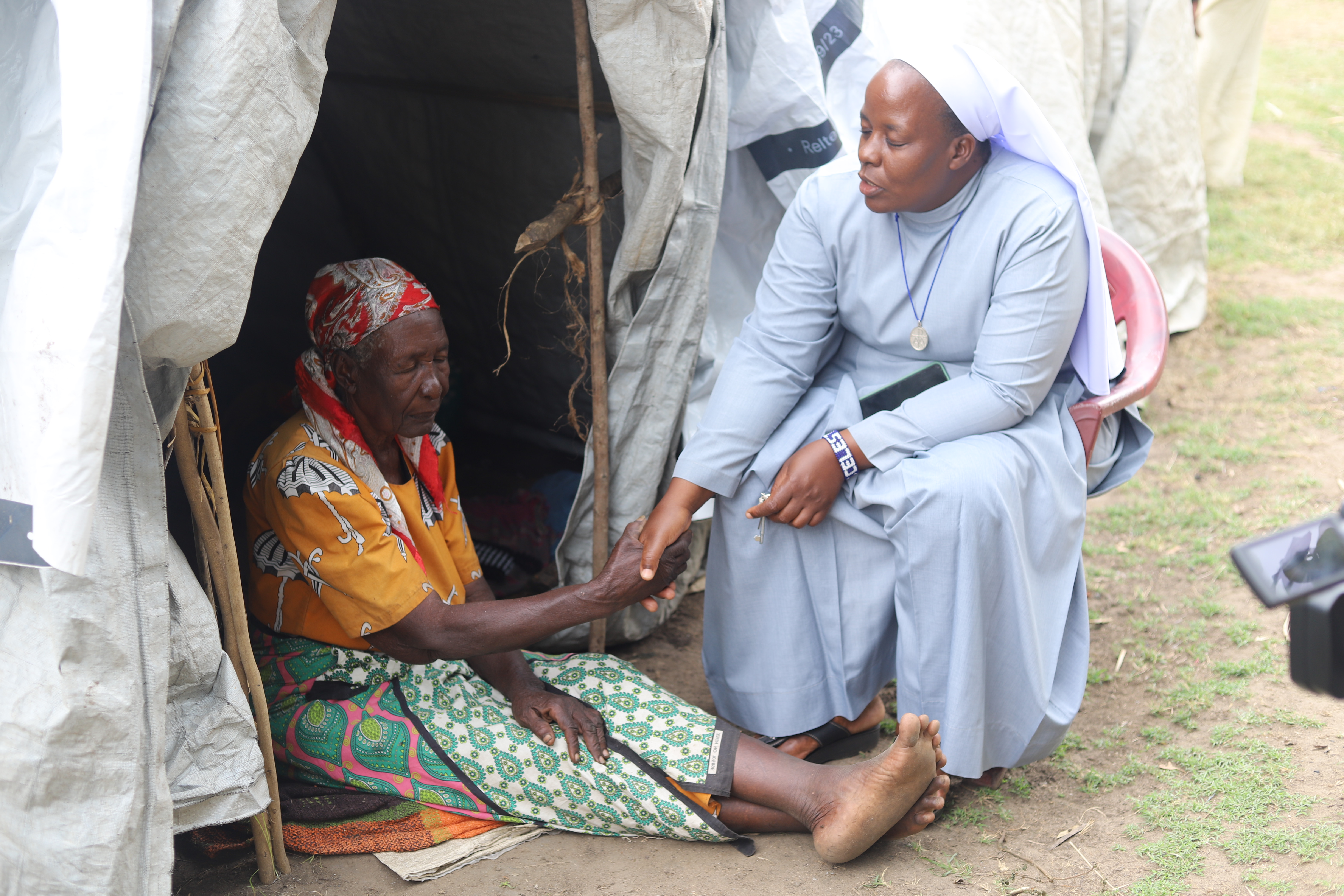 Sr. Celestine Nelima prays for Rosemary Auma, 72, at her tent in Khumwanda displacement camp in Busia, a town in western Kenya. (GSR photo/Doreen Ajiambo)