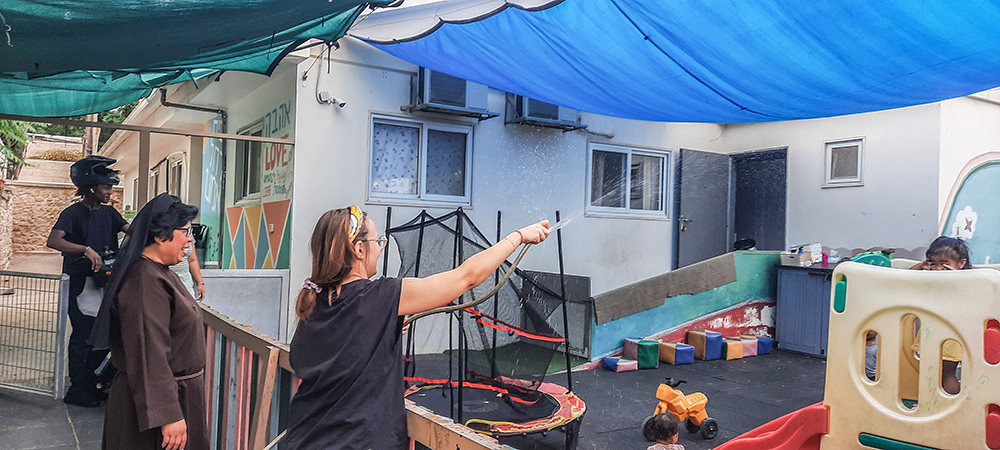 Sr. Maria David Magbanua looks on as a volunteer plays water games with the children at St. Rachel Center in Jerusalem on a hot summer afternoon. (Judith Sudilovsky)