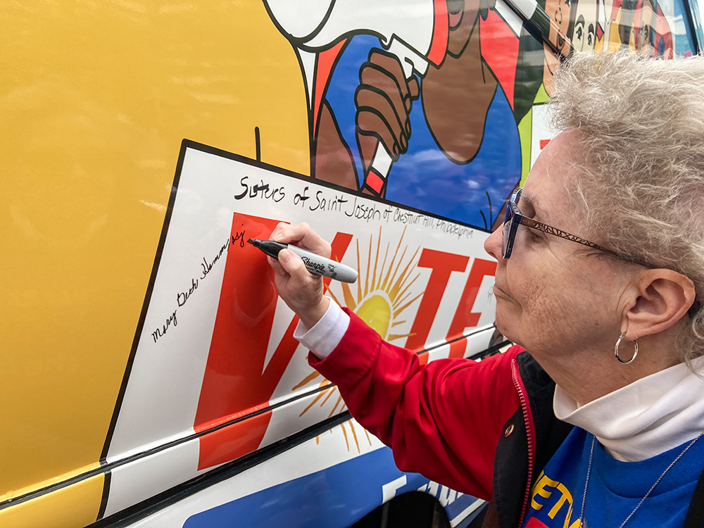 St. Joseph Sr. Mary Beth Hamm signs the bus at the Nuns on the Bus and Friends kickoff rally in Philadelphia Sept. 30. (GSR photo/Carol Zimmermann)