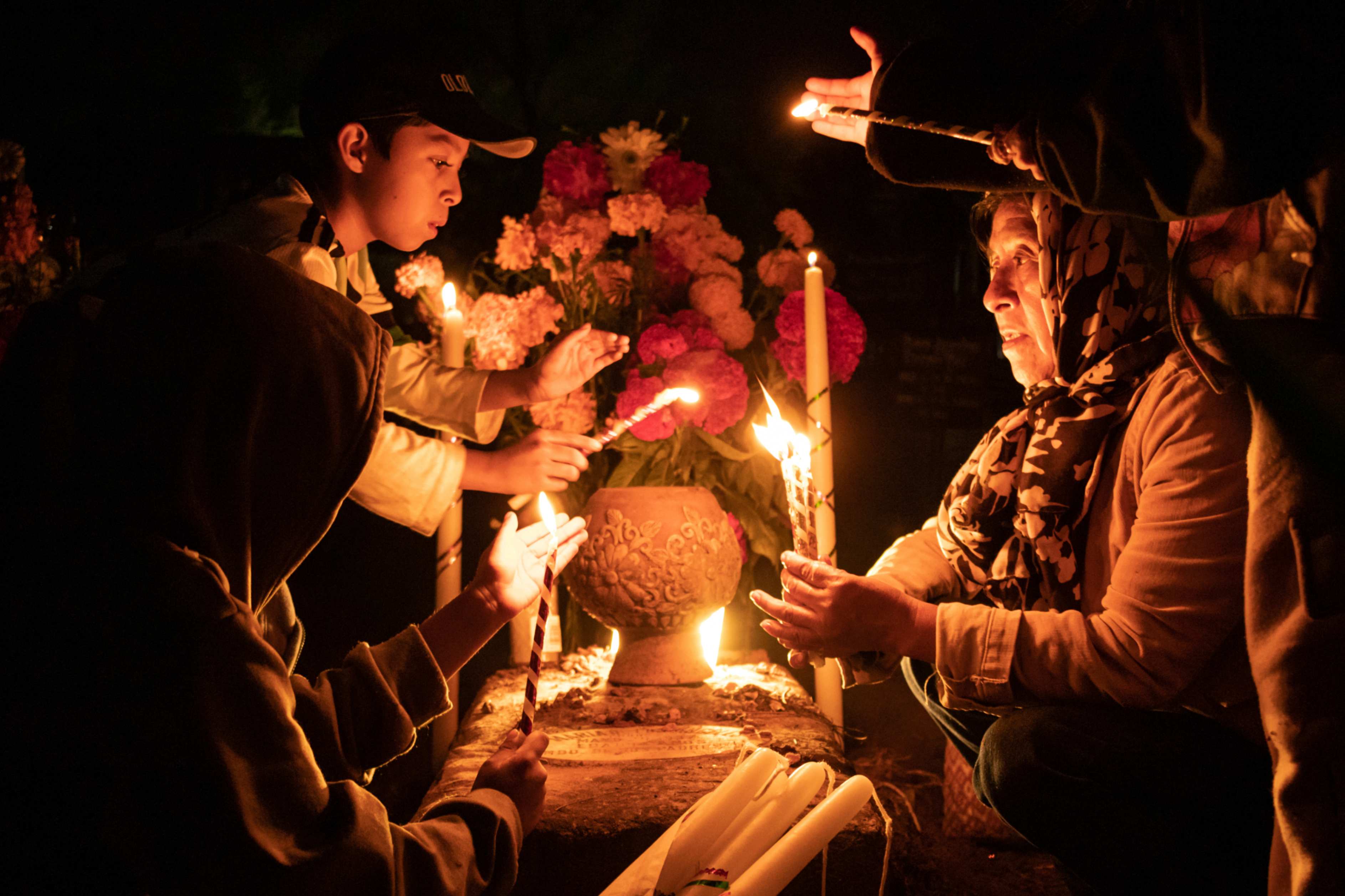 People hold candles over a tomb decorated with flowers at a cemetery in Atzompa, Mexico, Oct. 31, 2023. In a tradition that coincides with All Saints Day on Nov. 1 and All Souls Day on Nov. 2, families decorate graves with flowers and candles and spend the night in the cemetery, keeping company with their dearly departed. (AP/Maria Alferez)