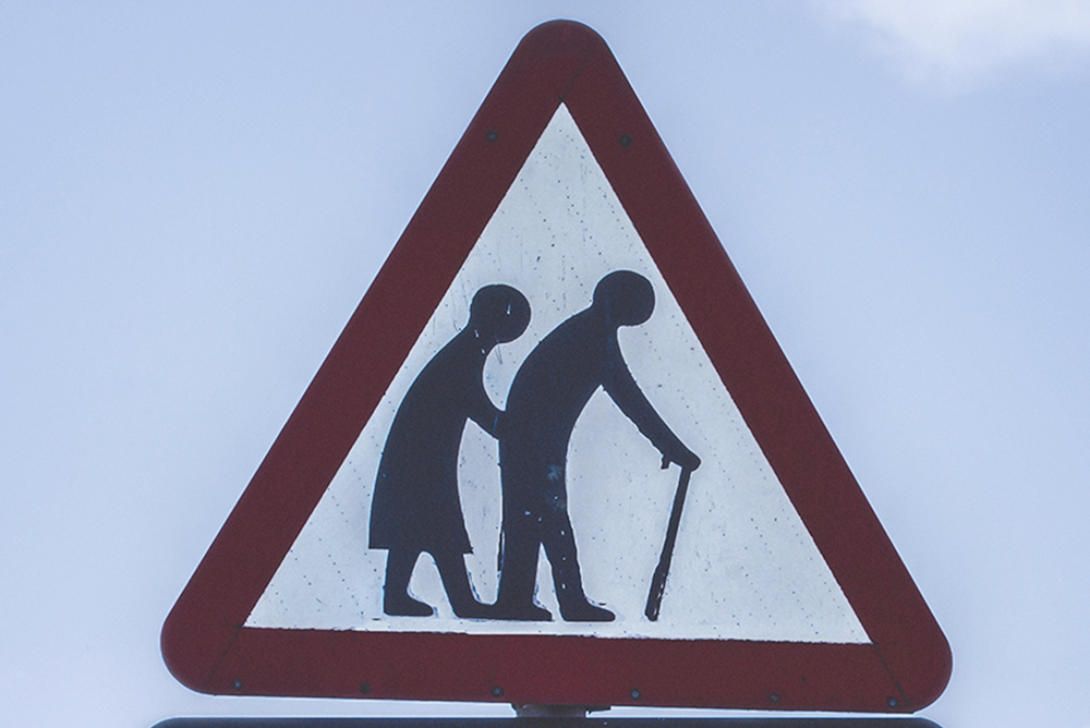 A crossing sign with two people, one with a cane (Unsplash/K Mitch Hodge)