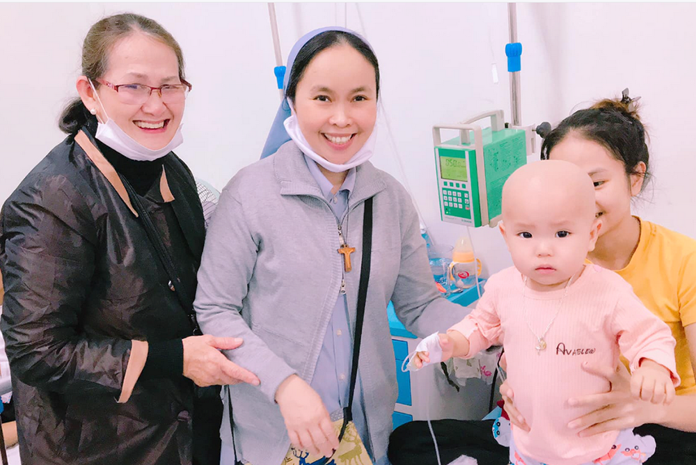 Daughters of Mary of Immaculate Conception Sr. Mary Theresa Ngo Thi Hong, center, and a volunteer visit a child with leukemia at the Central Hospital in Hue on Dec. 19. (Joachim Pham)