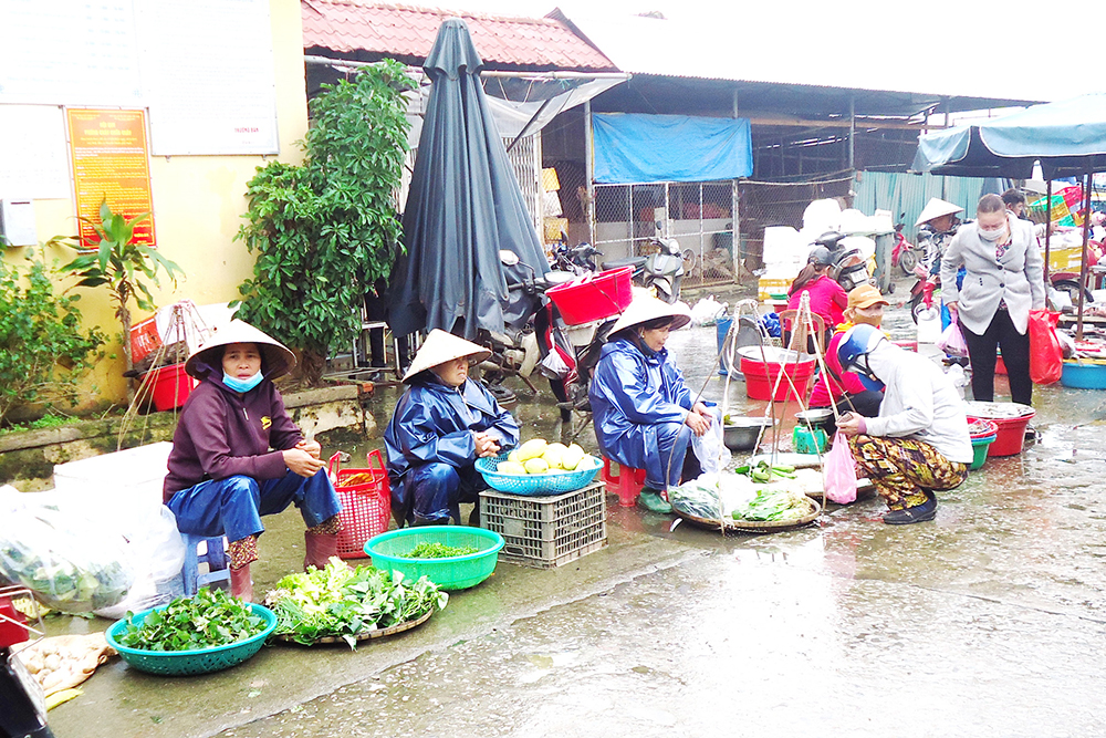 Women sell vegetables in rainy, bitter weather along the road to Dong Ba Market in Hue on Dec. 22. Tran Thi Nu, left, said her income dropped significantly due to the low number of buyers. (Joachim Pham)