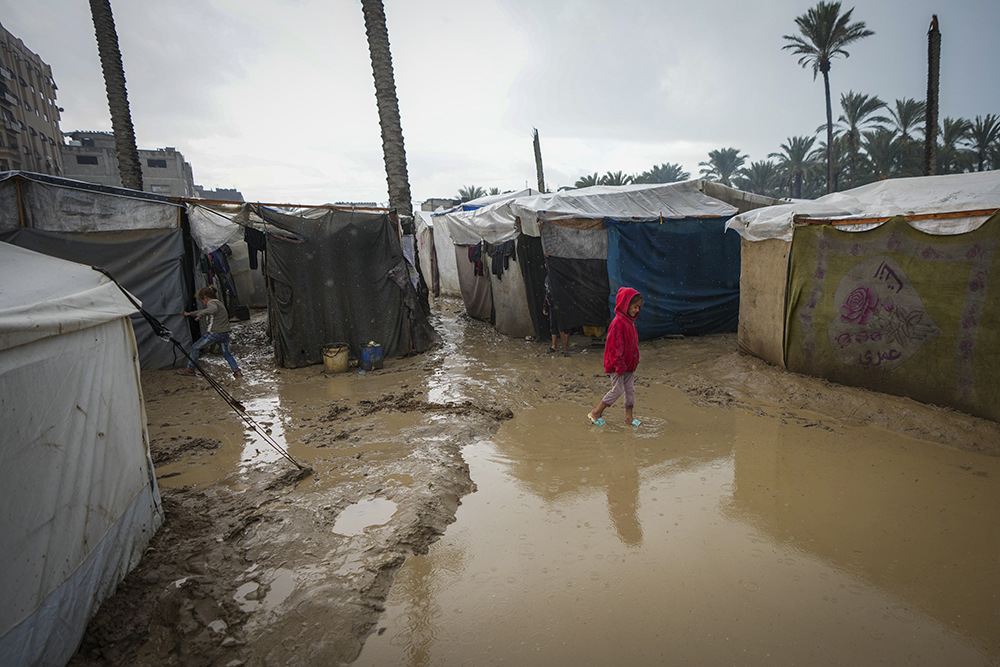 A young girl walks through a flooded street following overnight rainfall at the refugee tent camp for displaced Palestinians in Deir al-Balah, central Gaza Strip, Dec. 31, 2024. (AP/Abdel Kareem Hana)