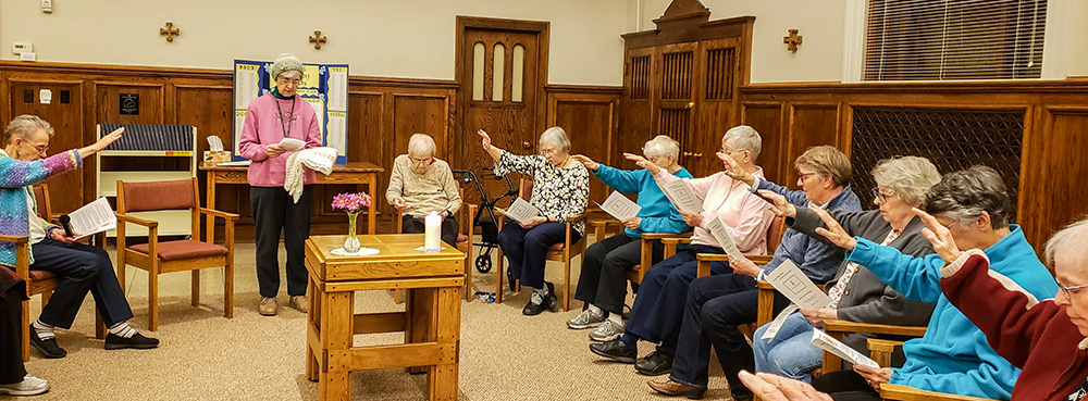 Las Hermanas de Notre Dame de Omaha, Nebraska, Estados Unidos, rezan por la Hna. Theresa Maly (tercera por la izquierda) en la ceremonia de su manto de oración, que se celebra cuando una hermana pasa a un centro asistencial. Se le entrega un chal que simboliza el amor y las oraciones de la comunidad por ella. (Foto: cortesía Hermanas de Notre Dame de Omaha)