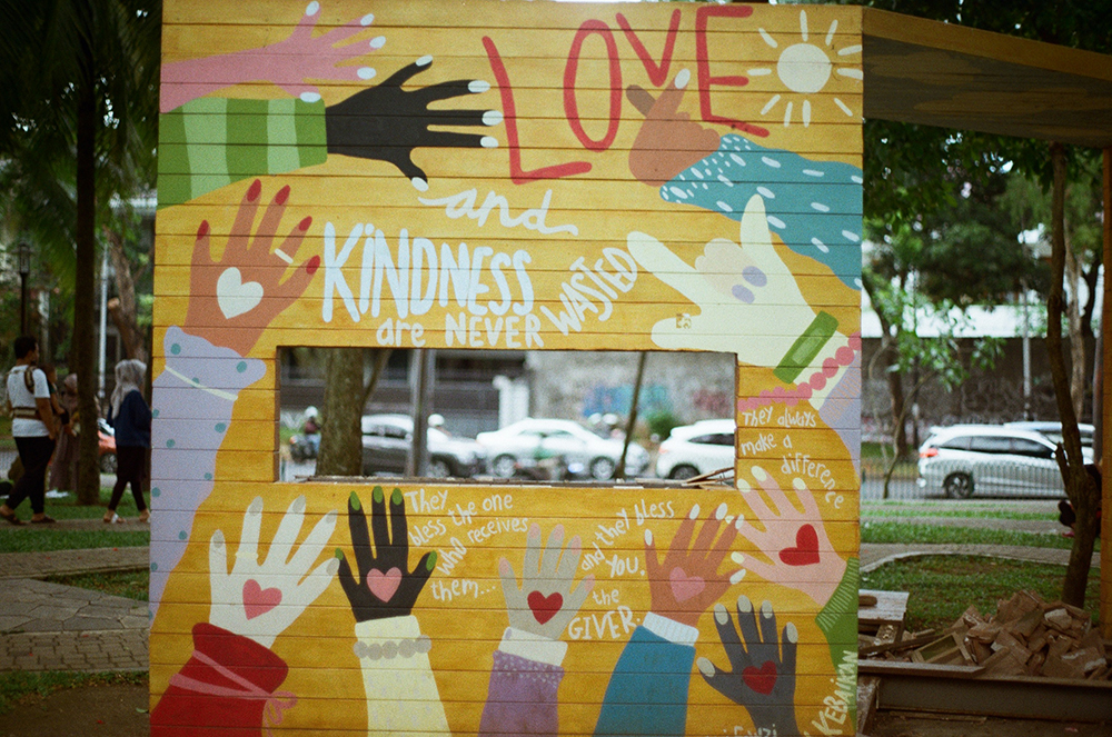 A yellow sign that says "Love, Kindess" with hands of different colors (Unsplash/Ditto Bowo)