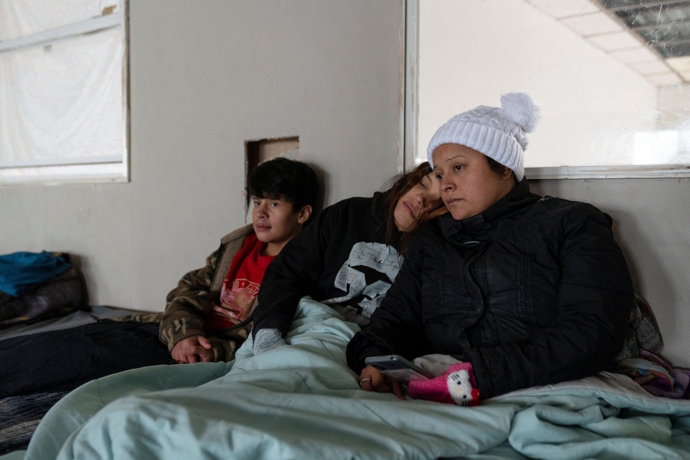 Mendez and children wear winter clothing and sit together beneath blanket.