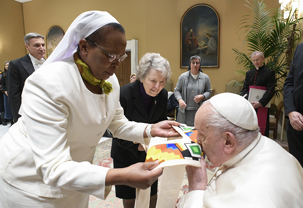 Pope Francis kisses a gift presented to him by Sr. Jane Wakahiu during an audience with the board of directors of the Conrad Hilton Foundation at the Vatican on Jan. 22. Standing to the right is Sr. Joyce Meyer, a member of the Presentation of the Blessed Virgin Mary, member of the foundation's board of directors, and international liaison to women religious for Global Sisters Report. (CNS/Vatican Media)