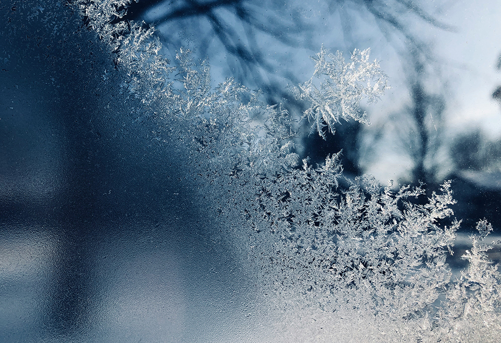 A closeup photo illustration shows frost and snowflakes against glass. (Unsplash/Sydney Rae)