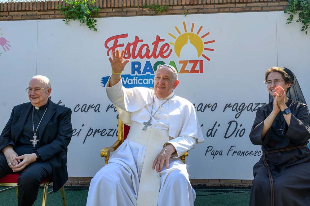 Pope sits in middle smiling and waving, Alzaga on left and Petrini on right.