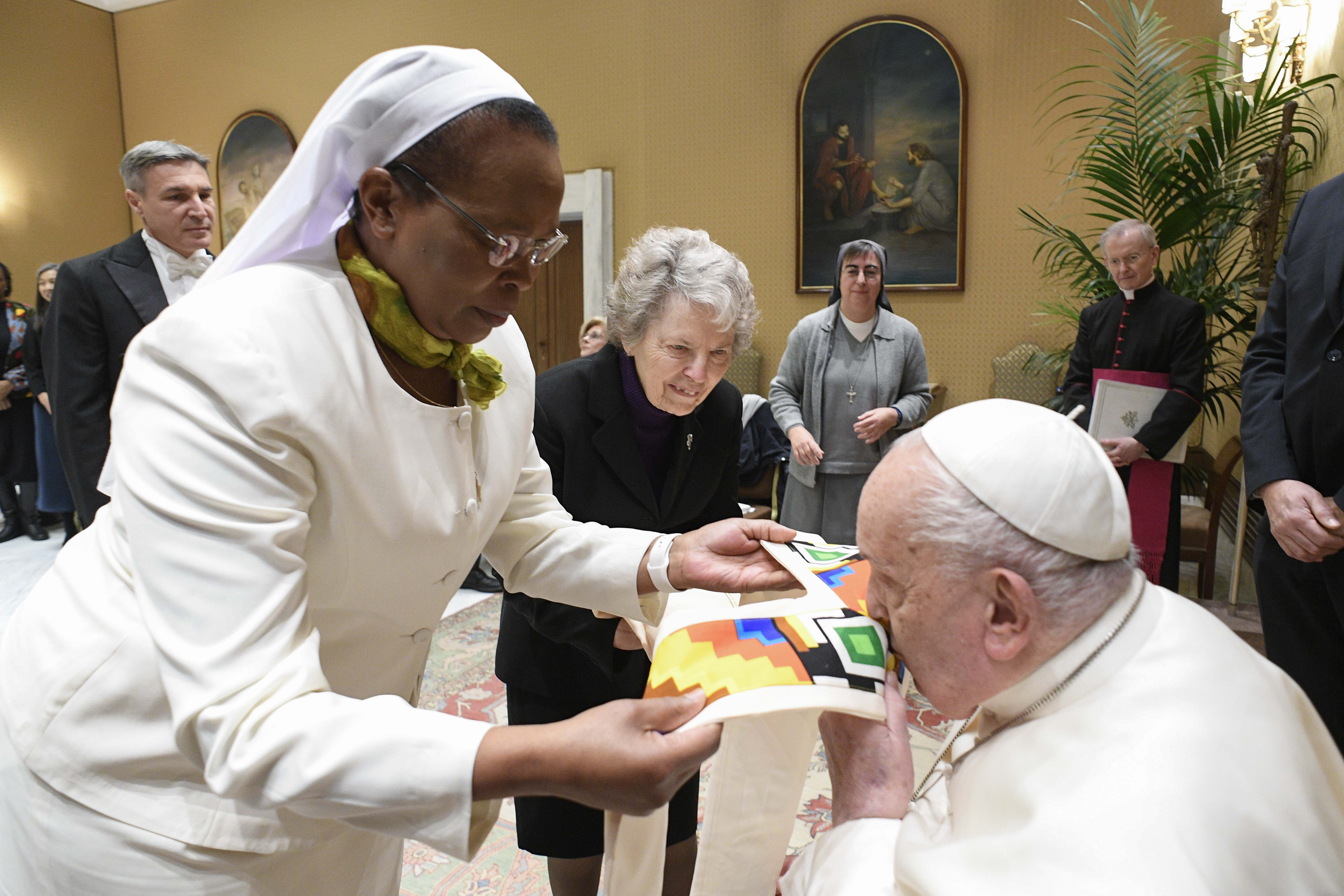 Pope Francis kisses a gift presented to him by Sr. Jane Wakahiu during an audience with the board of directors of the Conrad Hilton Foundation at the Vatican on Jan. 22, 2025. Standing to the right is Sr. Joyce Meyer.