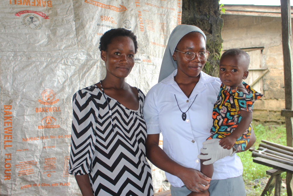 Sr. Janefrances Ihekuna (right) poses for a photo with a nursing mother and her baby after testing them for malaria and HIV during free medical outreach in the community.