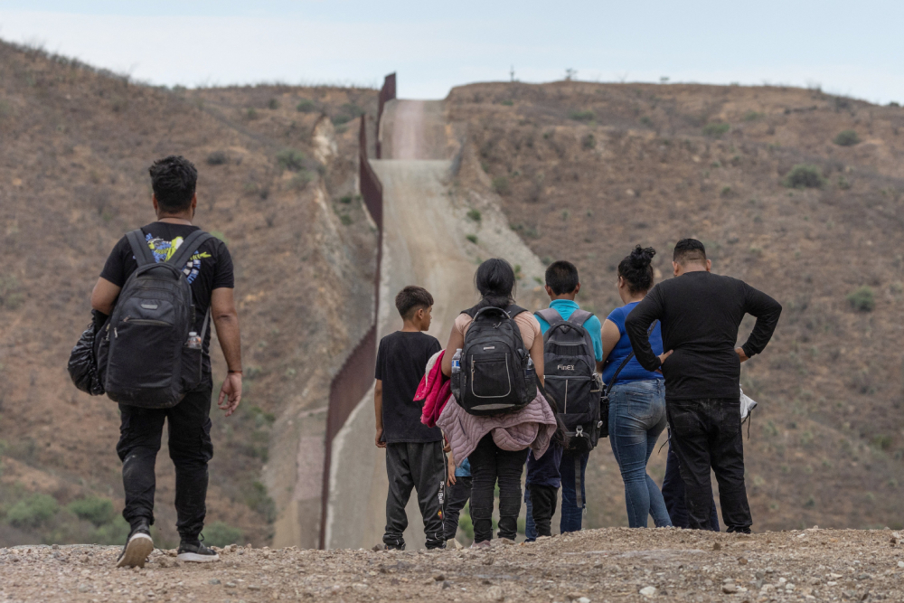 The wall at the U.S.-Mexico border is seen in the left side of the background as a group of migrants from South and Central America look to surrender to immigration officials after crossing into the United States from Mexico in Ruby, Arizona, June 24, 2024. (OSV News photo/Adrees Latif, Reuters)