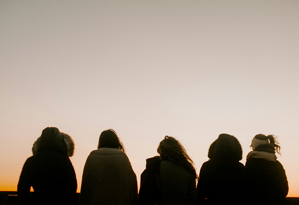 A group of people, backs turned, face toward a foggy horizon in an outdoor setting.  (Unsplash/Annie Williams)