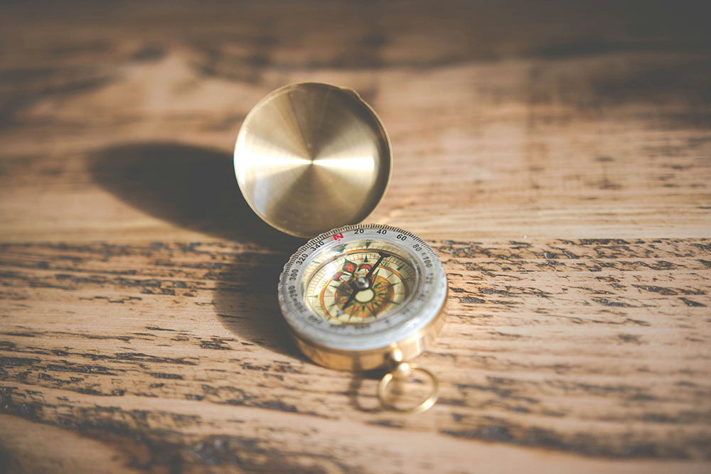 A golden compass on a wooden table (Unsplash/Chris Lawton)