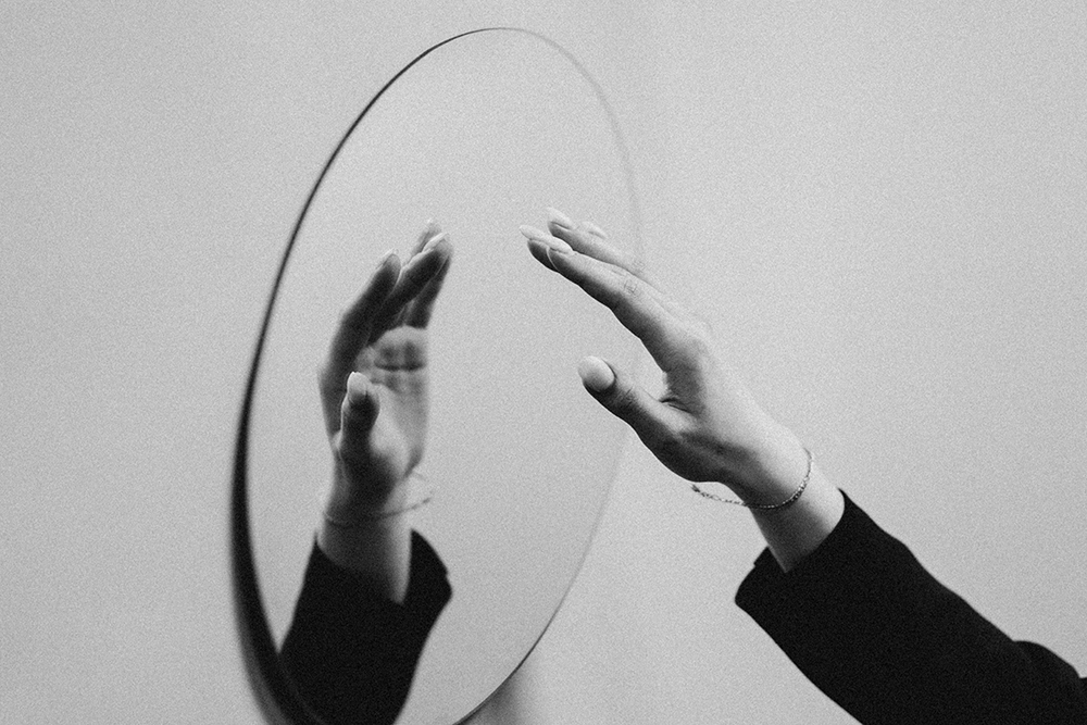 A mirror with a hand reflected in (Unsplash/Sekatsky)