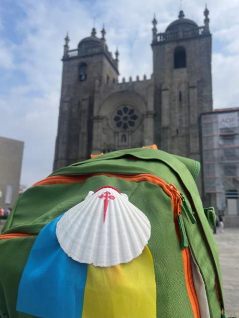 A backpack with the Ukrainian flag and Camino shell stands in front of Porto Cathedral