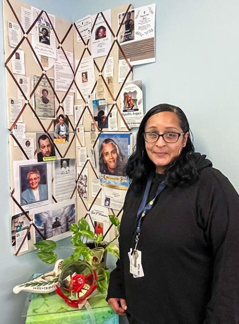 Darla Wharry stands in front of a collage featuring photographs and obituaries of St. Joseph's Place regulars who have died. (Sara Foss)