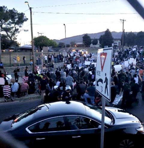 Protesters with paper signs stand in front of a line of armed police officers in riot gear May 31 at the El Paso, Texas, Police Department. (Celine Reinoso)