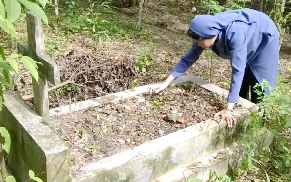 Daughters of Our Lady of the Visitation Sr. Martha Tran Thi Toan removes weeds from a neglected grave on Nov. 6. She is among  a group of nuns and volunteers who restore abandoned graves in rural villages in Huong Thuy town, Vietnam. (Joachim Pham) 