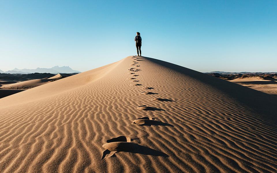 A person stands on top of a sand dune, with sunlight coming from the left of the photo.(Unsplash/NOEM)