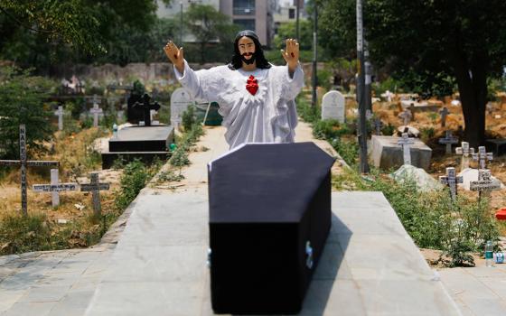 A statue of Jesus stands over the casket of a person who died after contracting COVID-19 before the burial at a graveyard in New Delhi on April 29, 2021. (CNS/Reuters/Adnan Abidi)