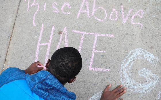 A boy writes a message on a sidewalk May 18 in Buffalo, New York, where a mass shooting took place May 14 at a Tops supermarket. (CNS/Reuters/Brendan McDermid)