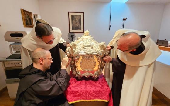 Three men religion in habits bend down to look at elaborate silver coffin.