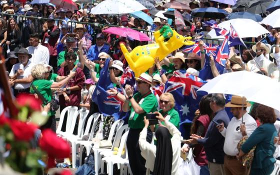 Many people stand from plastic chairs cheering and waving flags etc.