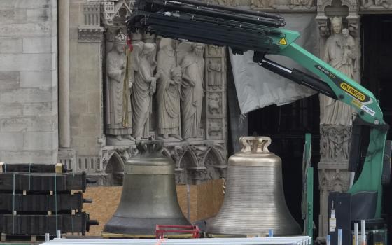 Large bronze bells on truck bed; in background is ornately carved portion of Cathedral exterior. 