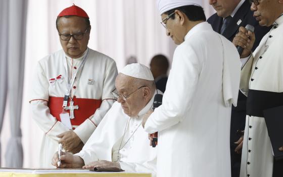 Pope Francis, center, flanked by the grand imam of Istiqlal Mosque Nasaruddin Umar, second right, and Archbishop of Jakarta Cardinal Ignatius Suharyo, left, signs a plate as he arrives at the Istiqlal Mosque for an interreligious meeting in Jakarta Thursday, Sept. 5, 2024. (Mast Irham/Pool Photo via AP)