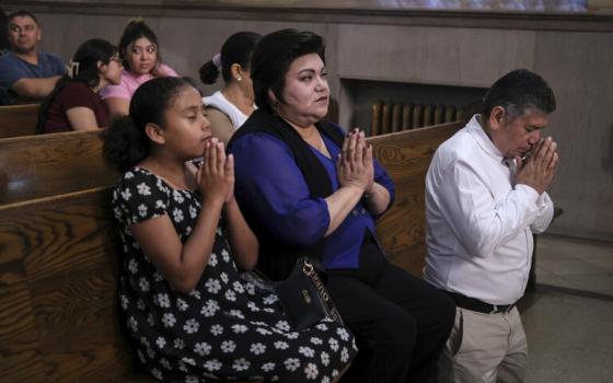 Woman, man, and young girl pray in front pew of church.