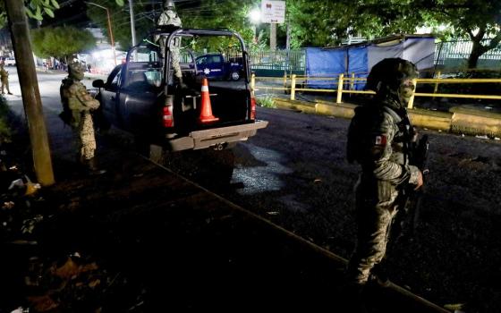 Two armed soldiers stand in a street at night.